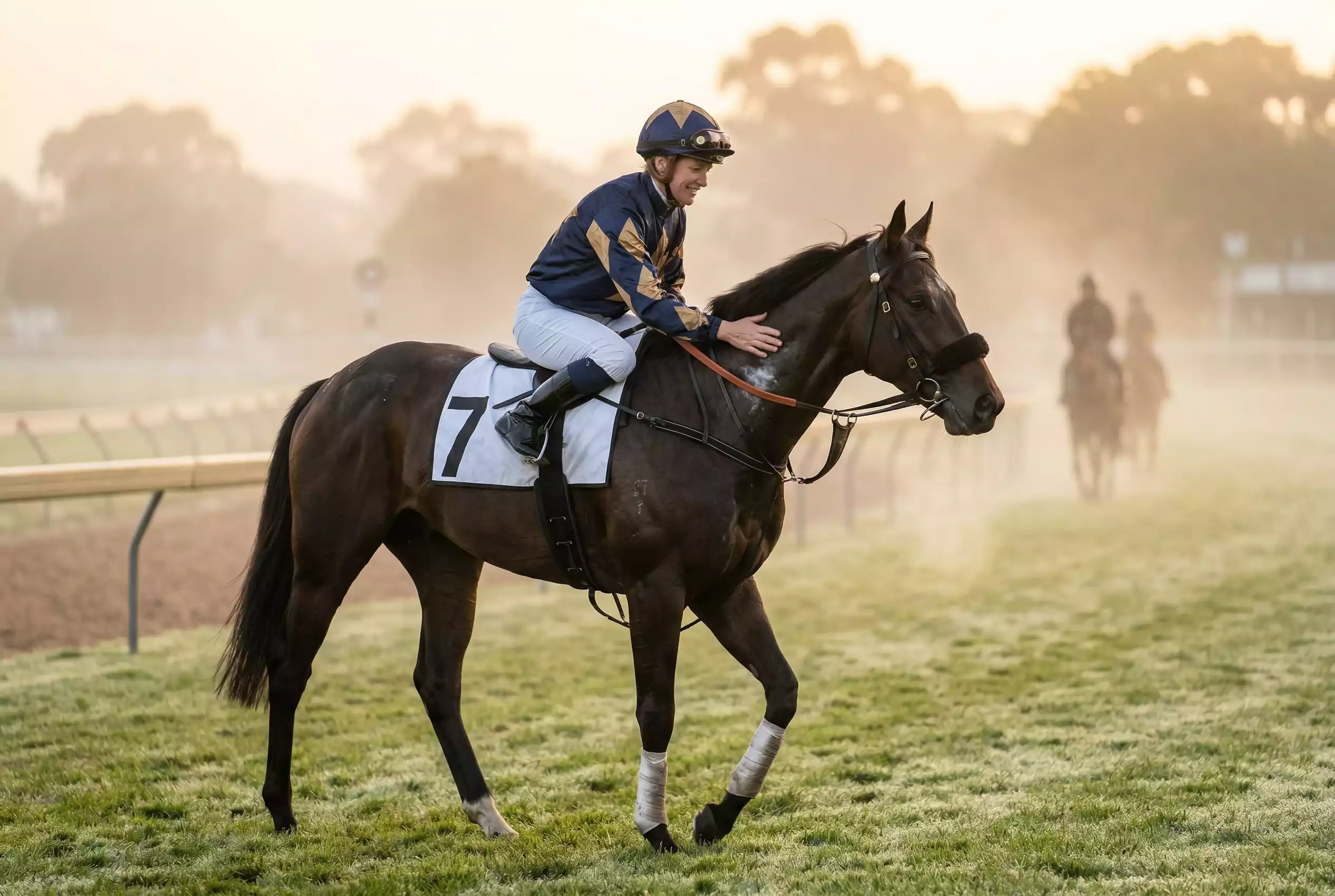 Jóquei montado em cavalo puro-sangue durante treino matinal em pista de grama